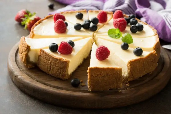 Pyszna tarta sernikowa z malinami i borówkami na drewnianej desce.