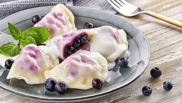 Pyszne pierogi z jagodami, polane śmietaną, z miętą i świeżymi owocami. Idealny przepis na lato!