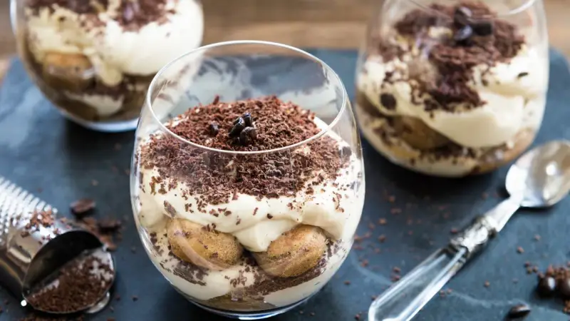 Pyszne tiramisu bez pieczenia w szklankach, udekorowane startą czekoladą i ziarnami kawy. Idealne na deser.